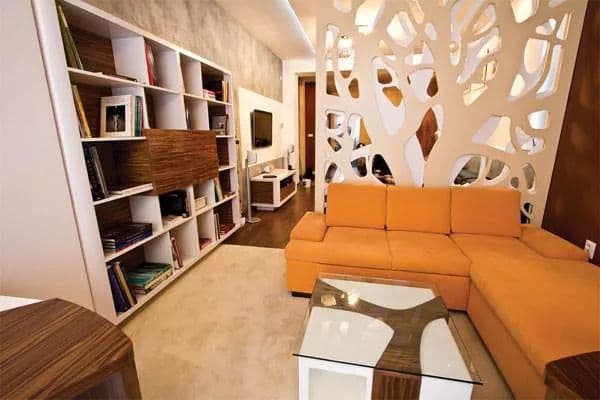 Modern living room with orange sectional sofa, white shelving, and decorative wall design. Stylish and contemporary decor.