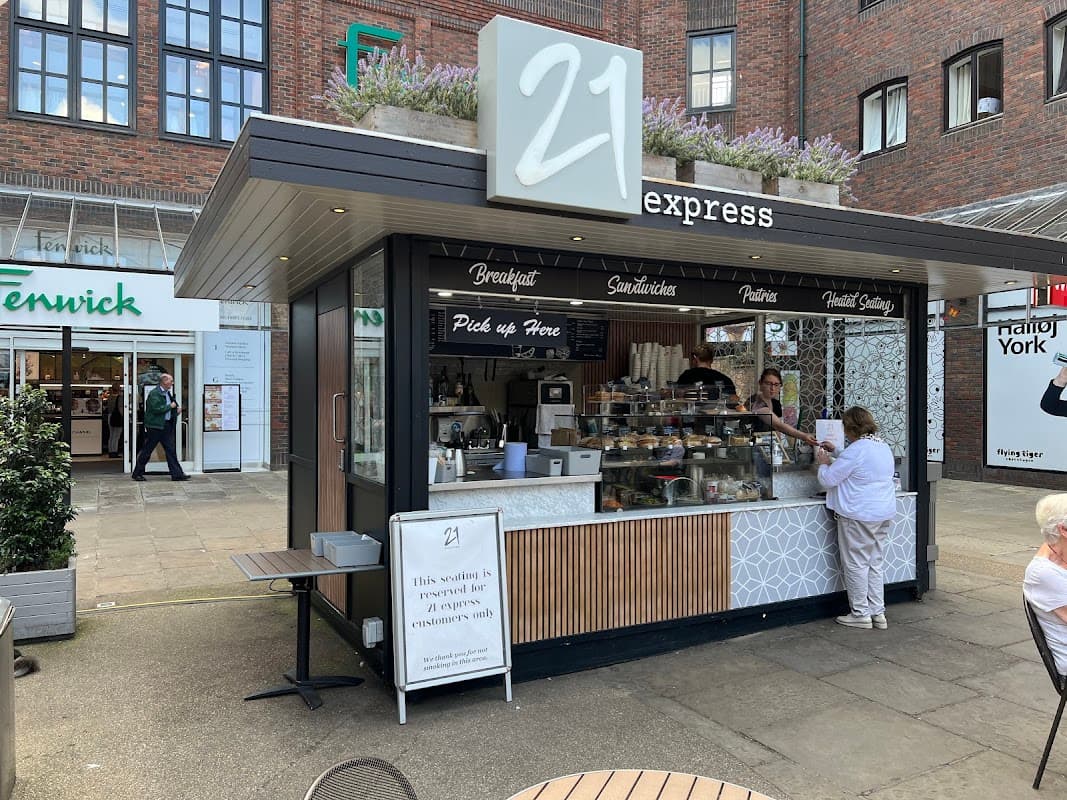 Modern food kiosk with a sign reading "21 express," offering breakfast, sandwiches, and pastries in a shopping area.
