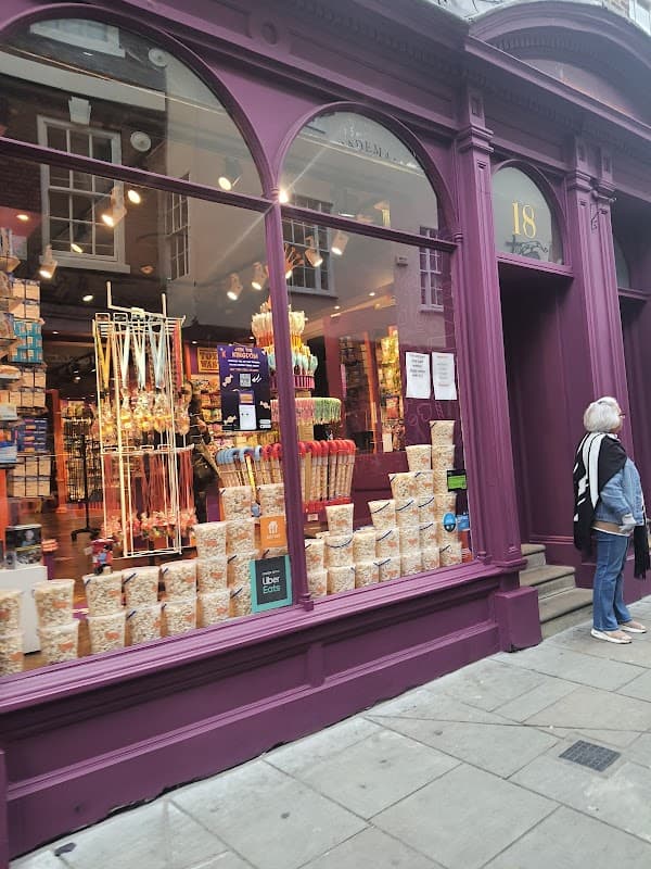 Colorful shop window displaying various candies and snacks, with a woman standing nearby on a cobbled street.