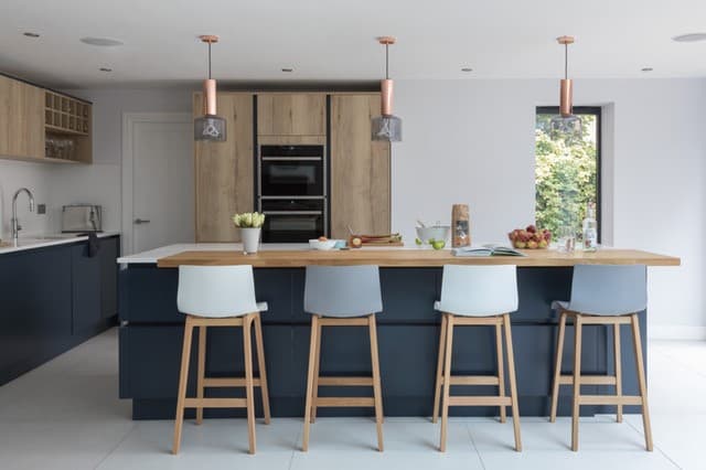 Modern kitchen with a wooden island, bar stools, sleek cabinetry, and pendant lights, featuring fresh fruits and decor.