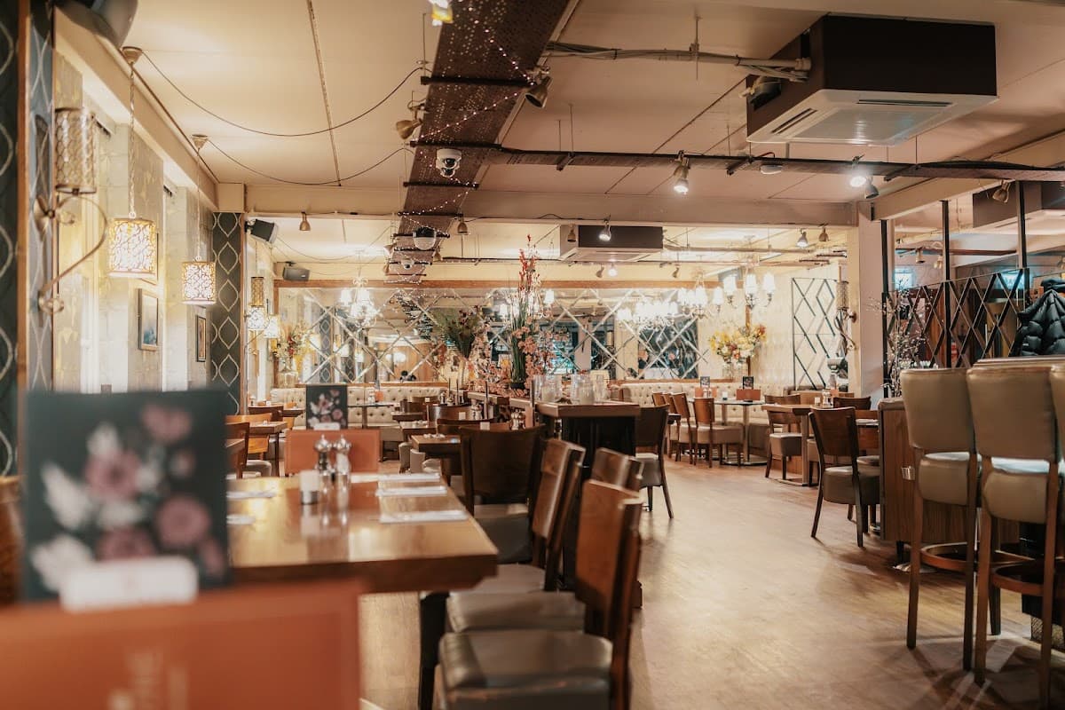 Elegant dining area with wooden tables, plush chairs, decorative lighting, and floral arrangements in a cozy atmosphere.