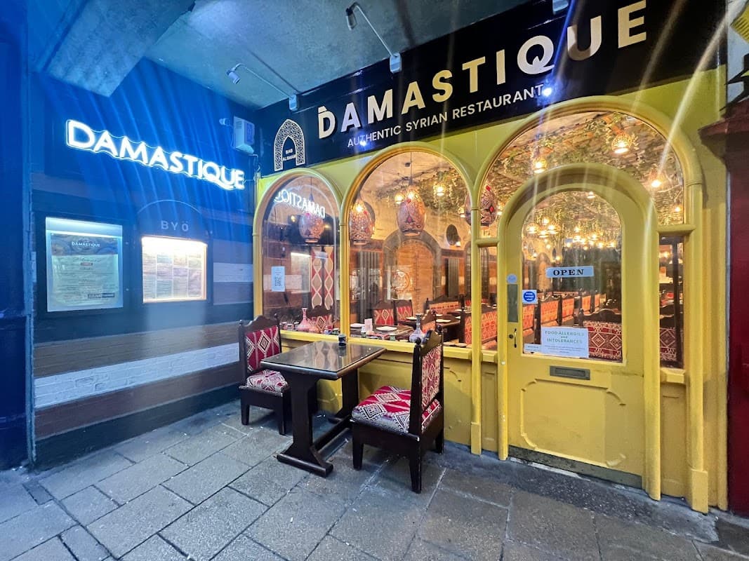 Charming restaurant entrance with yellow arches, warm lighting, and ornate decor, featuring outdoor seating.