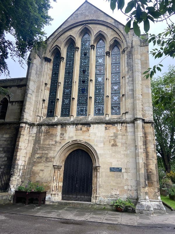 Historic building with large stained glass windows and a decorative stone entrance, surrounded by greenery.
