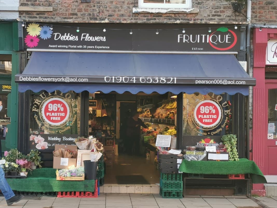 Colorful flower displays outside "Debbie's Flowers" shop, with signs promoting plastic-free products and a welcoming entrance.
