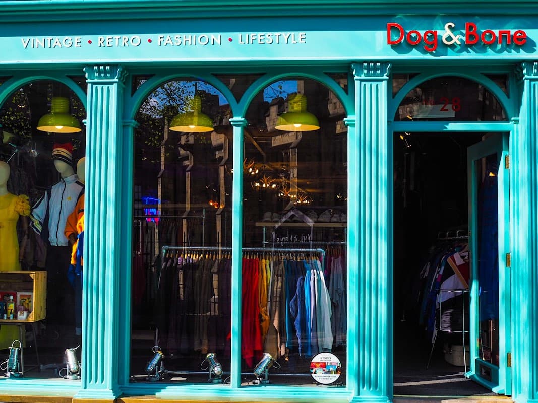 Vintage clothing shop with teal facade, arched windows, colorful garments displayed, and bright green pendant lights.