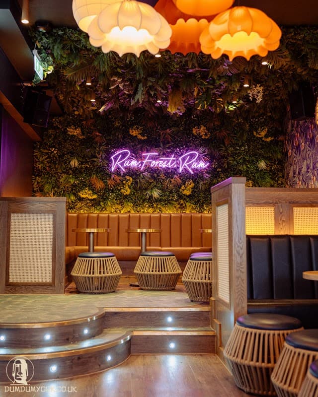 Cozy bar interior with tropical decor, neon sign, wooden seating, and stylish pendant lights.