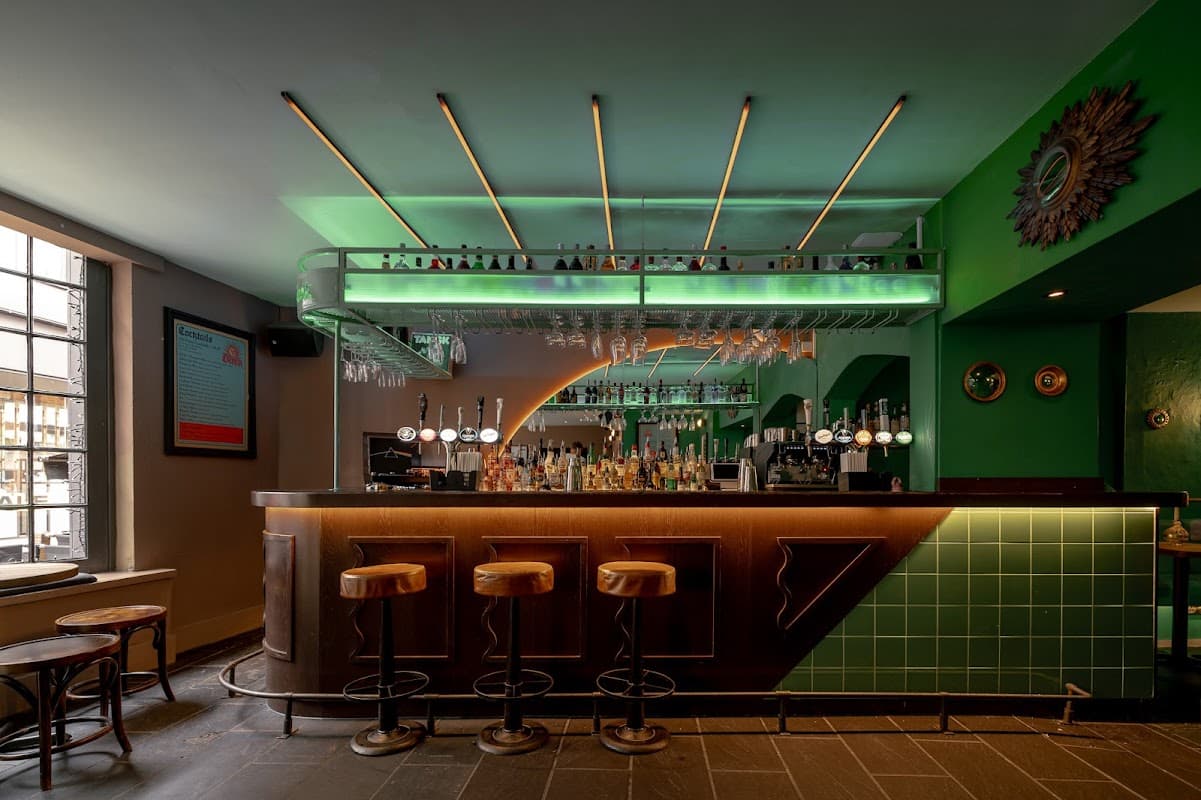 Stylish bar with a green and wooden interior, illuminated shelves, and bar stools against a modern backdrop.