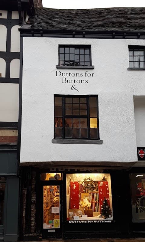 Hobby shop exterior with "Duttons For Buttons" sign, large window displaying craft supplies, and festive decorations.
