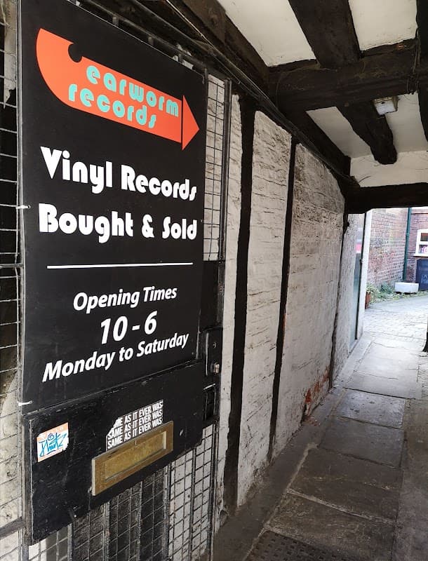 Sign for Earworm Records with vinyl records listed, opening times, and a narrow pathway leading to the shop.