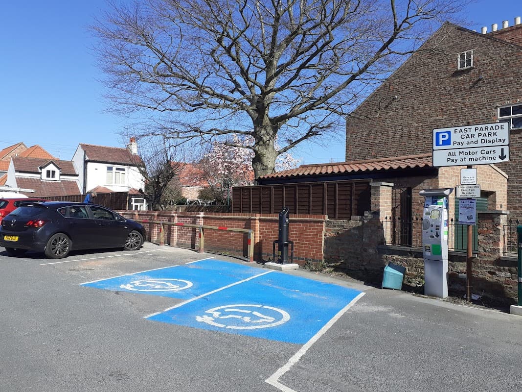 East Parade Car Park with marked disabled spaces, payment machine, and a large tree nearby, set against residential buildings.