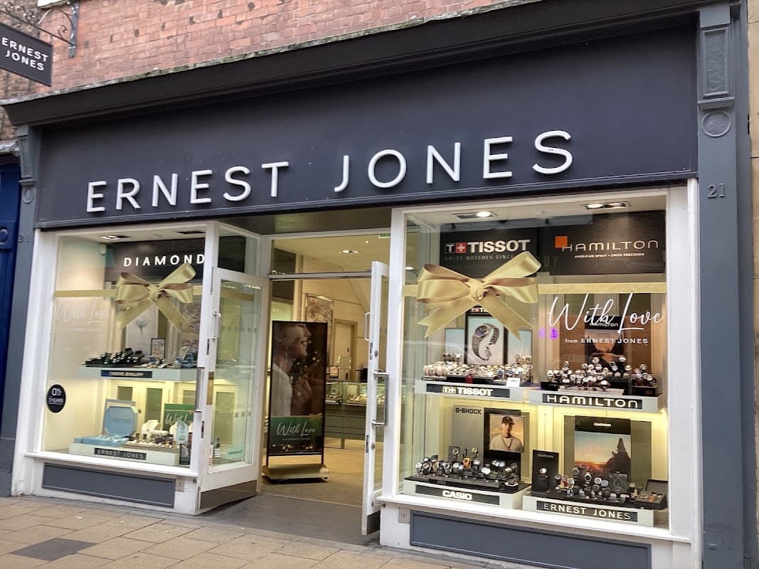 Storefront of Ernest Jones jewellers featuring watches, jewelry displays, and a large bow decoration.
