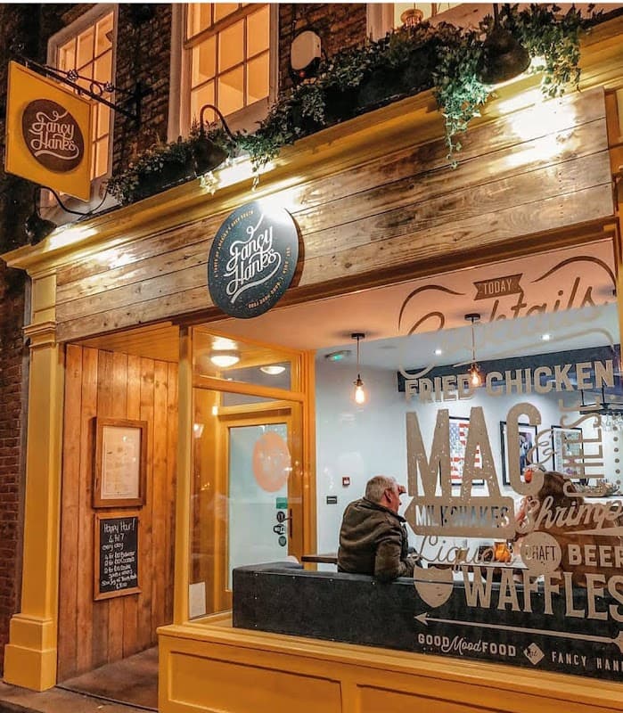 Brightly lit restaurant entrance with wooden accents, outdoor sign, and large glass windows showcasing diners inside.