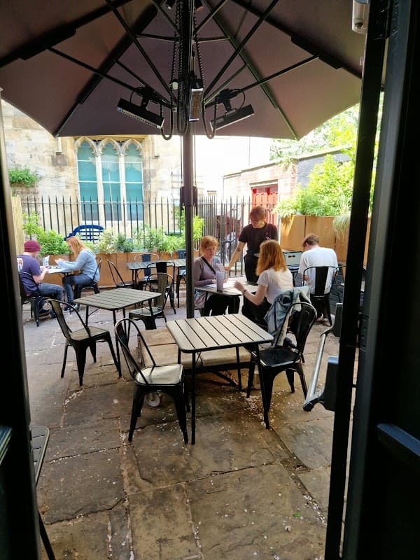 Outdoor seating area with tables and chairs, patrons dining, and a large umbrella in a charming courtyard setting.