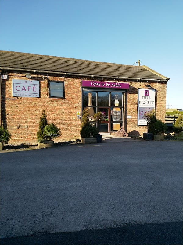 Brick building with "Field & Fawcett" signage, large glass entrance, and potted plants on either side.