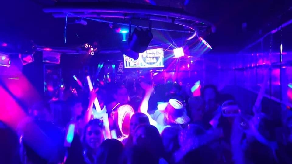 Vibrant nightclub scene with colorful lights, dancing crowd, and glowing accessories in a lively atmosphere.