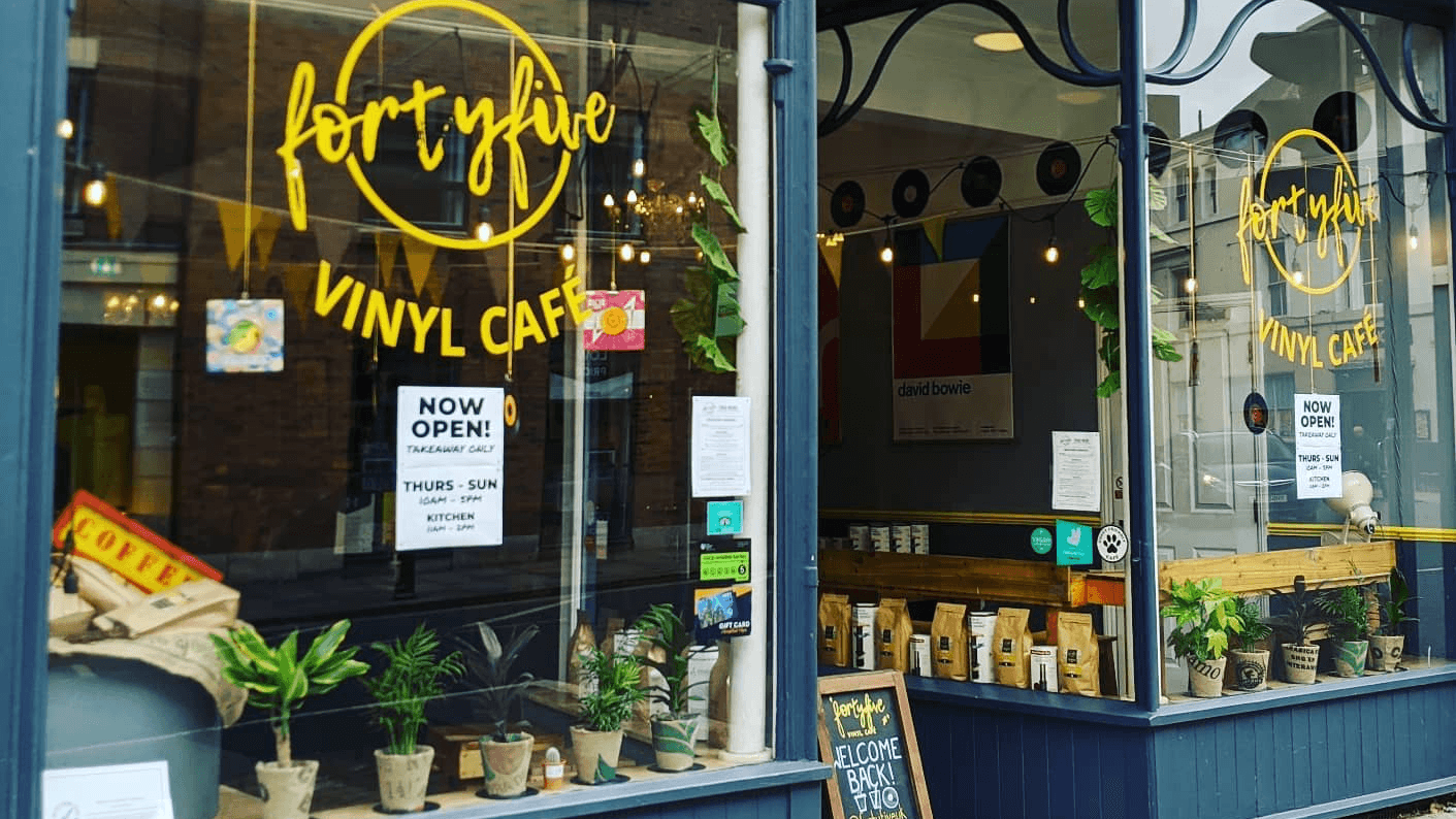 Vinyl café storefront with large windows, plants, and a sign announcing "NOW OPEN" in York, Yorkshire.
