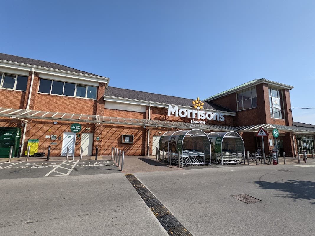 Morrisons supermarket entrance at Foss Island Retail Park, with shopping carts and clear blue sky above.