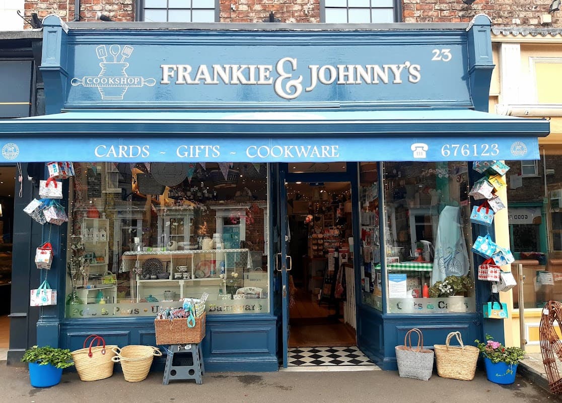 Quaint shopfront of Frankie & Johnny's Cookshop, featuring gifts, cards, and cookware, with colorful displays and baskets.