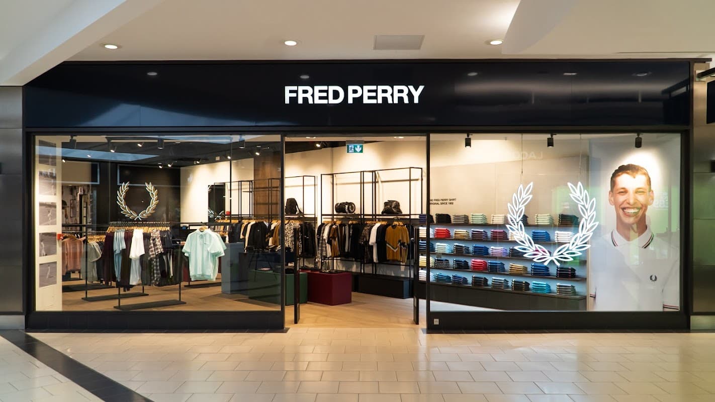 FRED PERRY outlet store front featuring clothing displays and a large logo with a smiling model on the side.