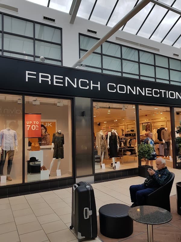 French Connection storefront with large signage, showcasing clothing displays and a customer seated nearby.