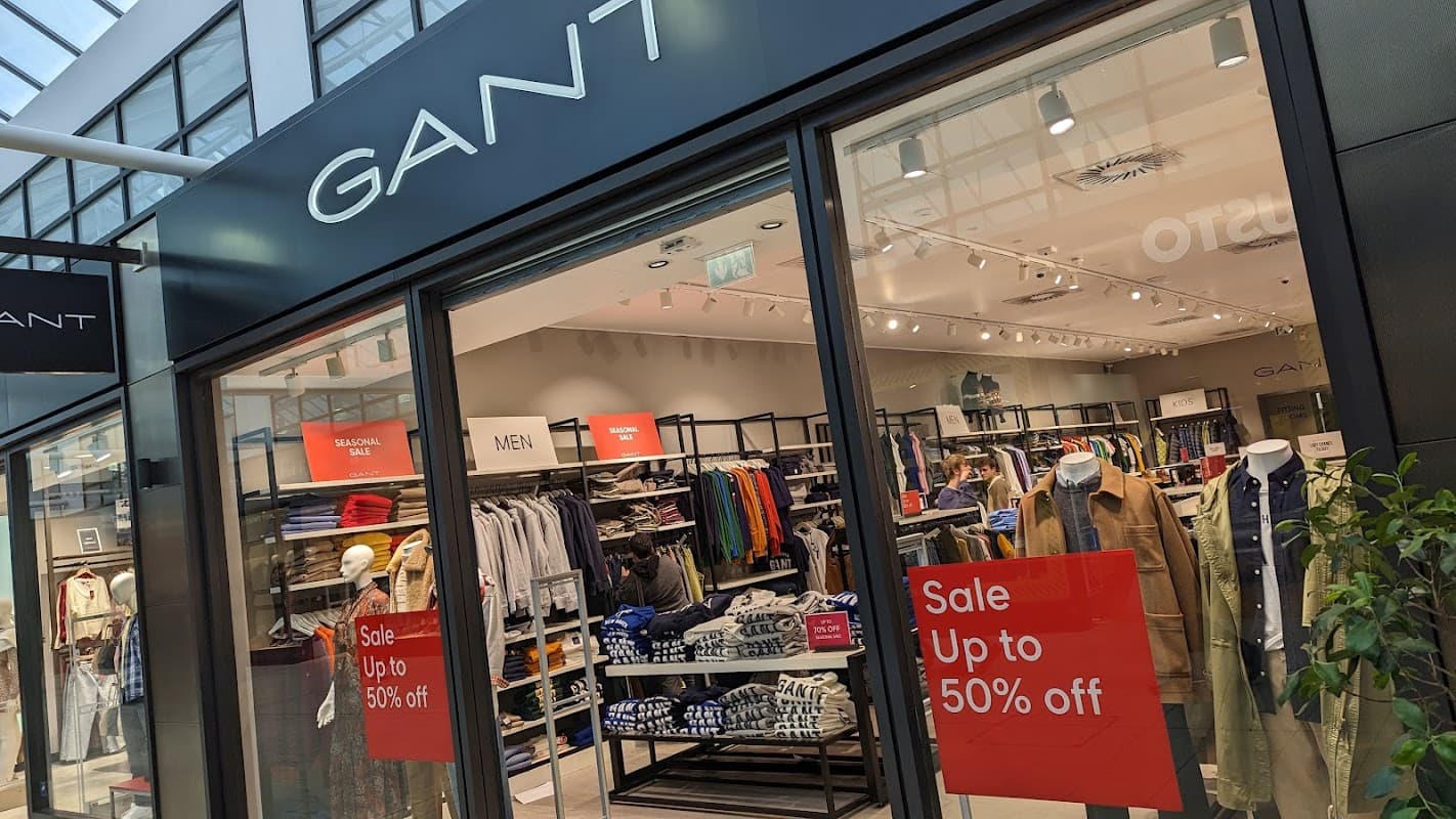 GANT Outlet storefront with sale signs, showcasing men's clothing and accessories inside a modern shopping center.