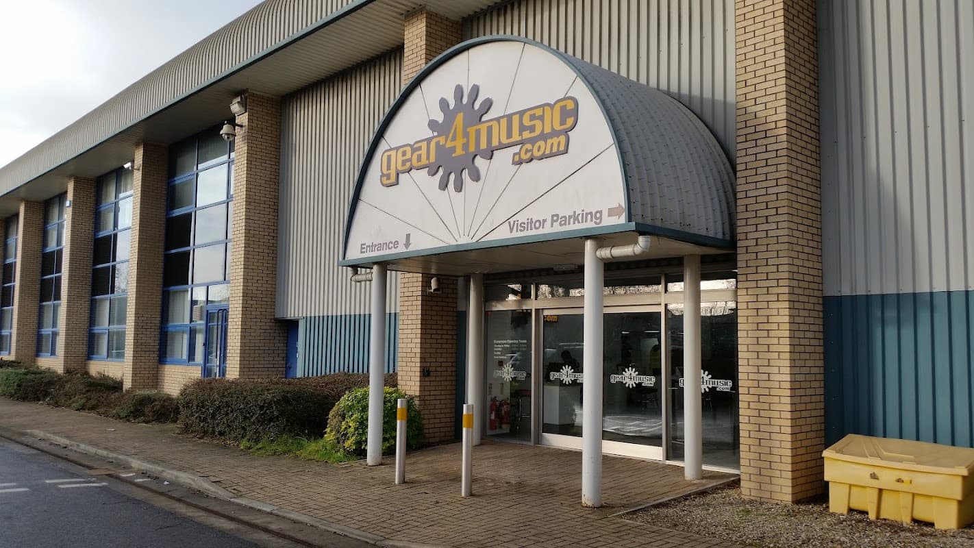Entrance of Gear4music shop with a curved awning, large glass doors, and visitor parking sign.