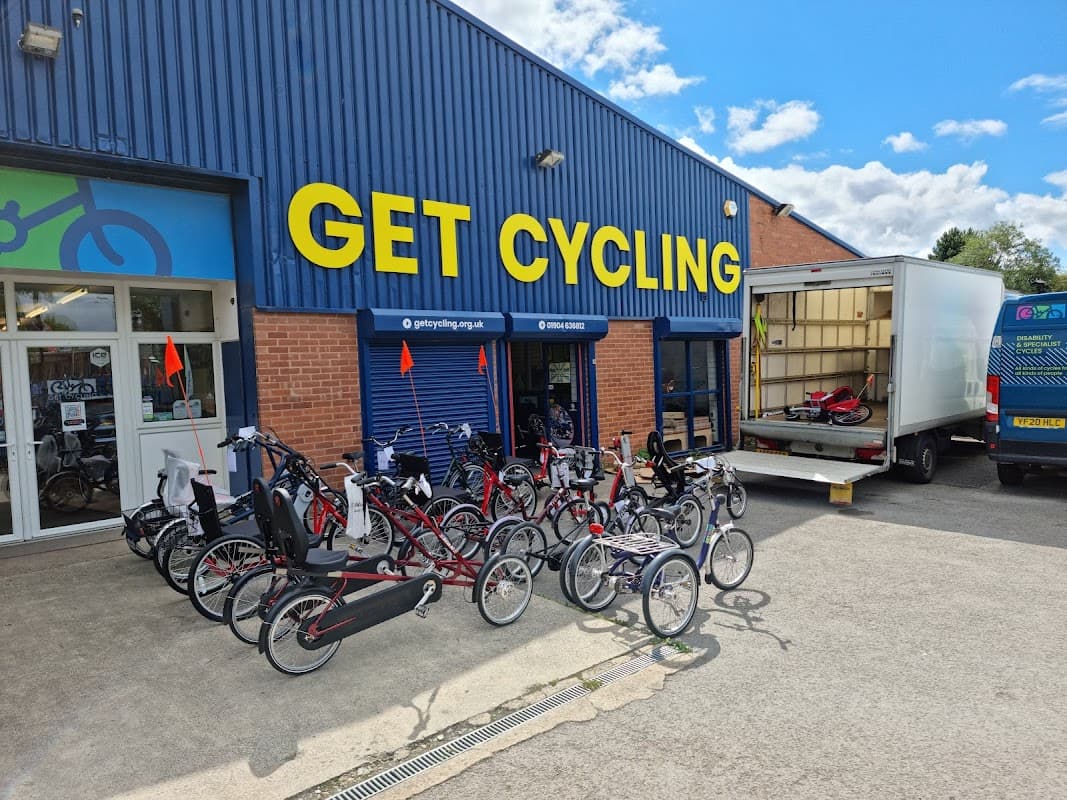 Bicycle shop exterior with various bikes displayed outside and a delivery truck parked nearby under a blue sky.