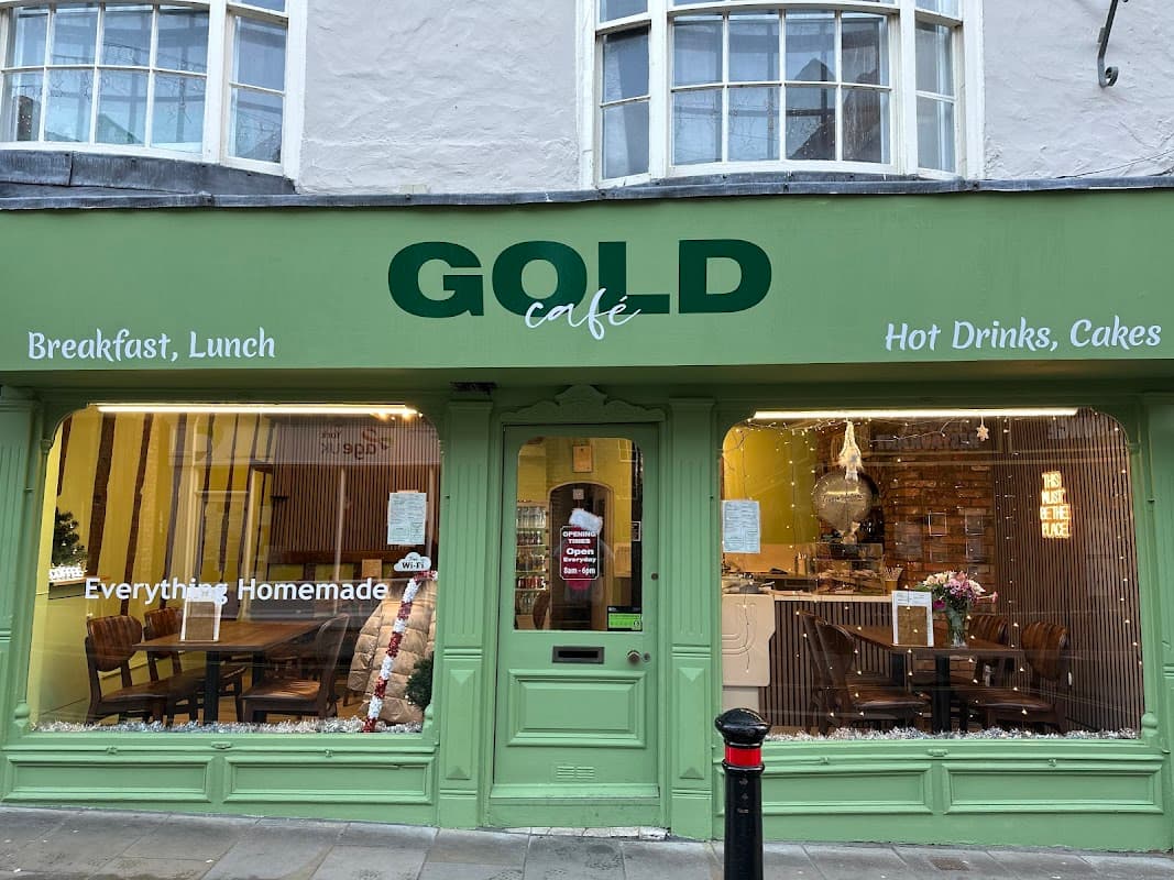 Green storefront of GOLD Café in York, featuring signs for breakfast, lunch, and homemade cakes. Warm, inviting atmosphere.