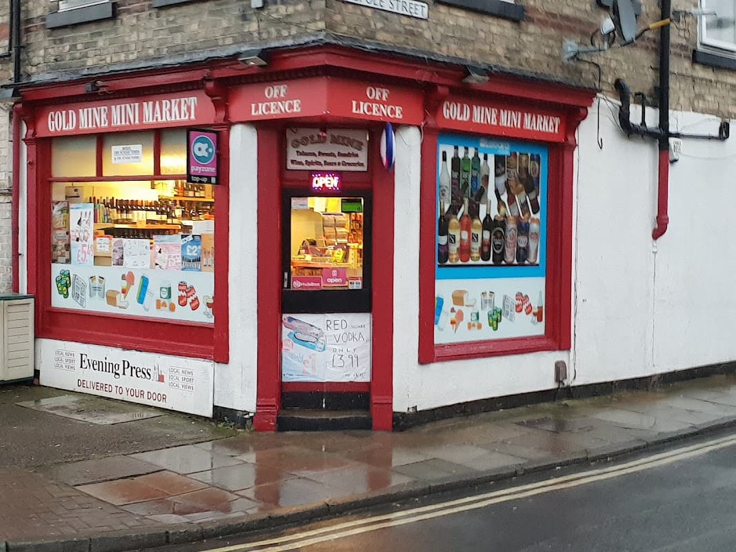 Gold Mine Mini Market storefront with red trim, displaying various beverages and snacks, and an "Open" sign.