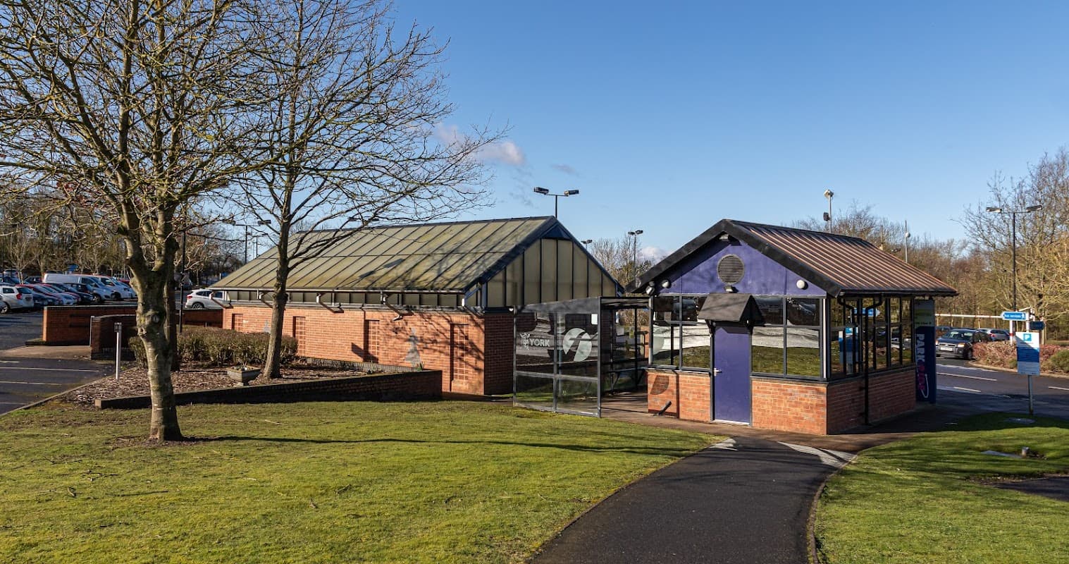 Grimston Bar Park & Ride with a modern shelter, grassy area, and parked cars under a clear blue sky.