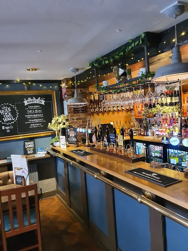 Cozy pub interior with a wooden bar, colorful drink displays, and a chalkboard menu in a warm, inviting atmosphere.