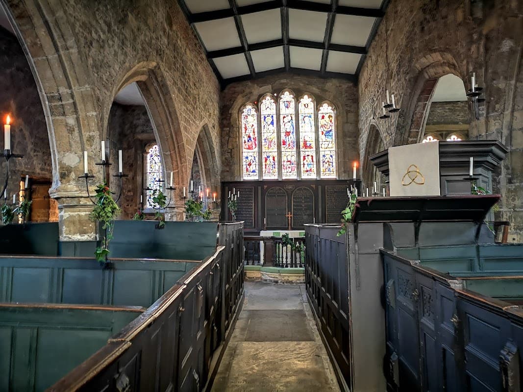 Interior of Holy Trinity Church featuring stained glass windows, stone walls, pews, and candlelit ambiance.