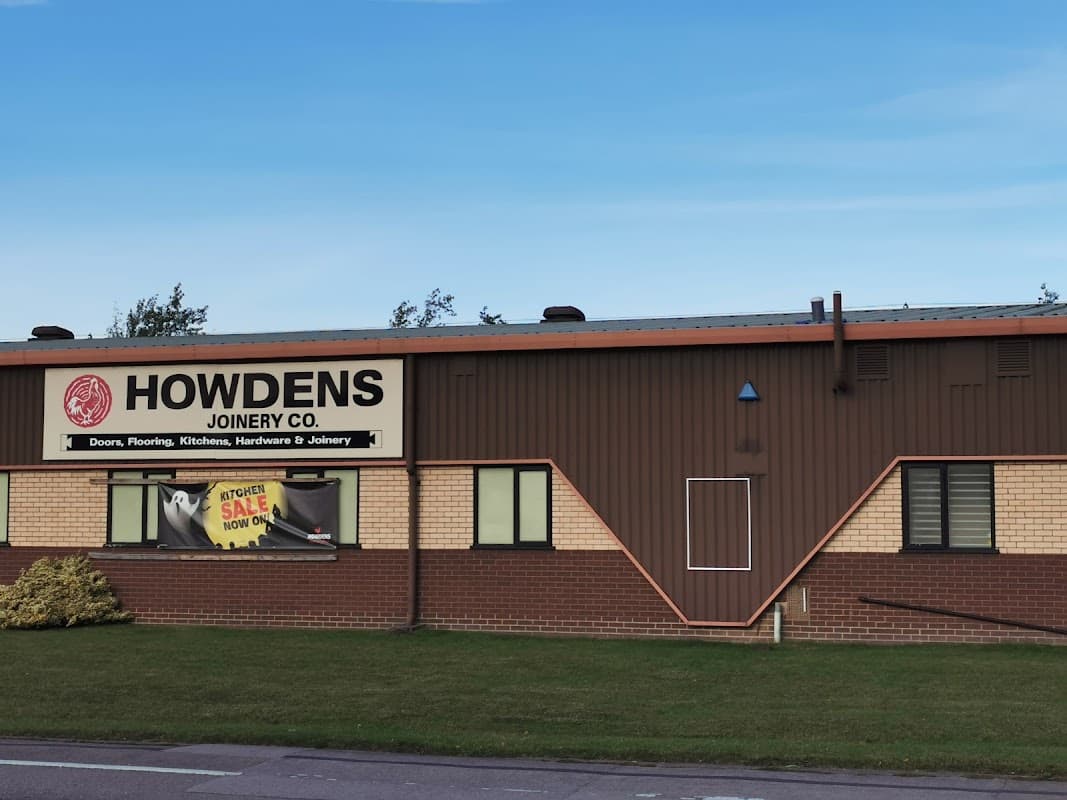 Howdens Joinery Co. building with signage, featuring a brick facade and a clear blue sky.