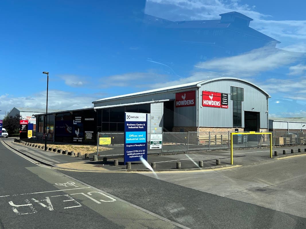 Howdens Ironmongers building in York, featuring signage and a fenced parking area along a street.