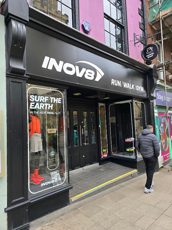 INOV8 store front featuring running shoes, colorful displays, and a customer outside in a gray jacket.
