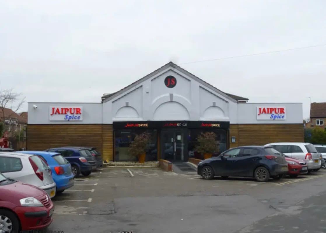 Jaipur Spice restaurant exterior with a modern design, featuring a sign, large windows, and parked cars in the lot.