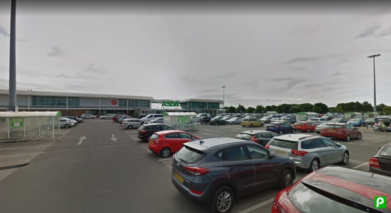 Busy Park & Ride area with numerous parked cars and an ASDA store in the background under a cloudy sky.