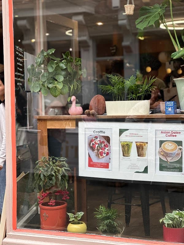 A cozy cafe window showcasing plants, colorful menu boards, and a pink flamingo decoration.