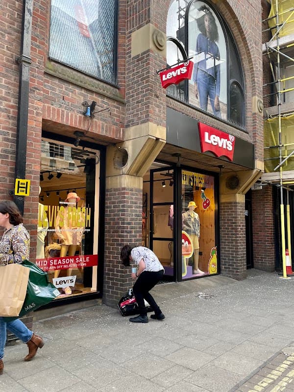Levi's store entrance with sale signage, shoppers outside, and a person crouching by the door in York.