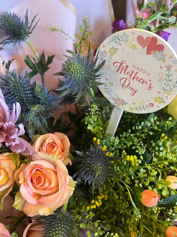Colorful bouquet featuring roses, thistles, and greenery with a "Happy Mother's Day" tag.