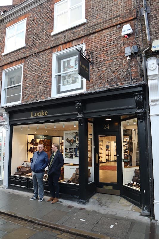 Loake Shoemakers storefront in York, with two men standing outside and a brick facade featuring large windows.