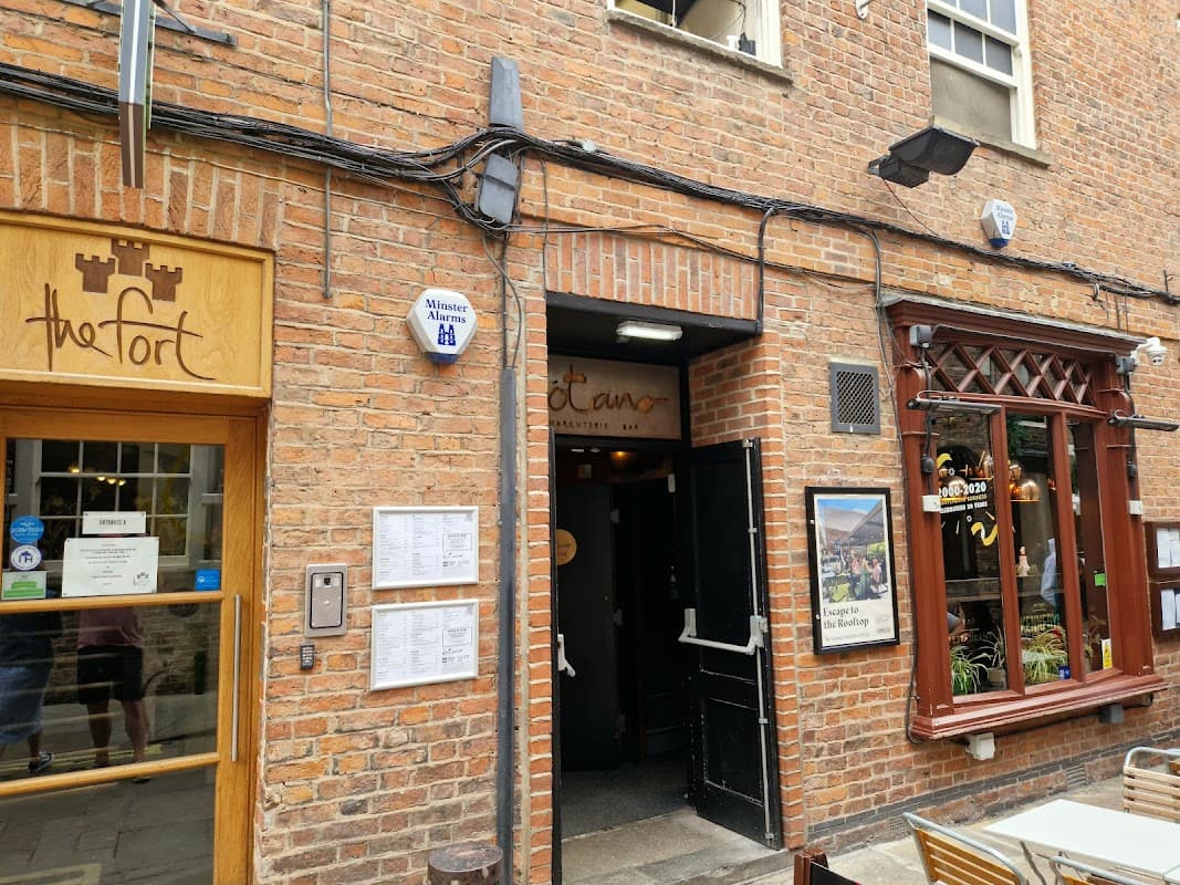 Entrance to Manahatta York pub, featuring a brick facade and wooden accents, with signage and outdoor seating visible.