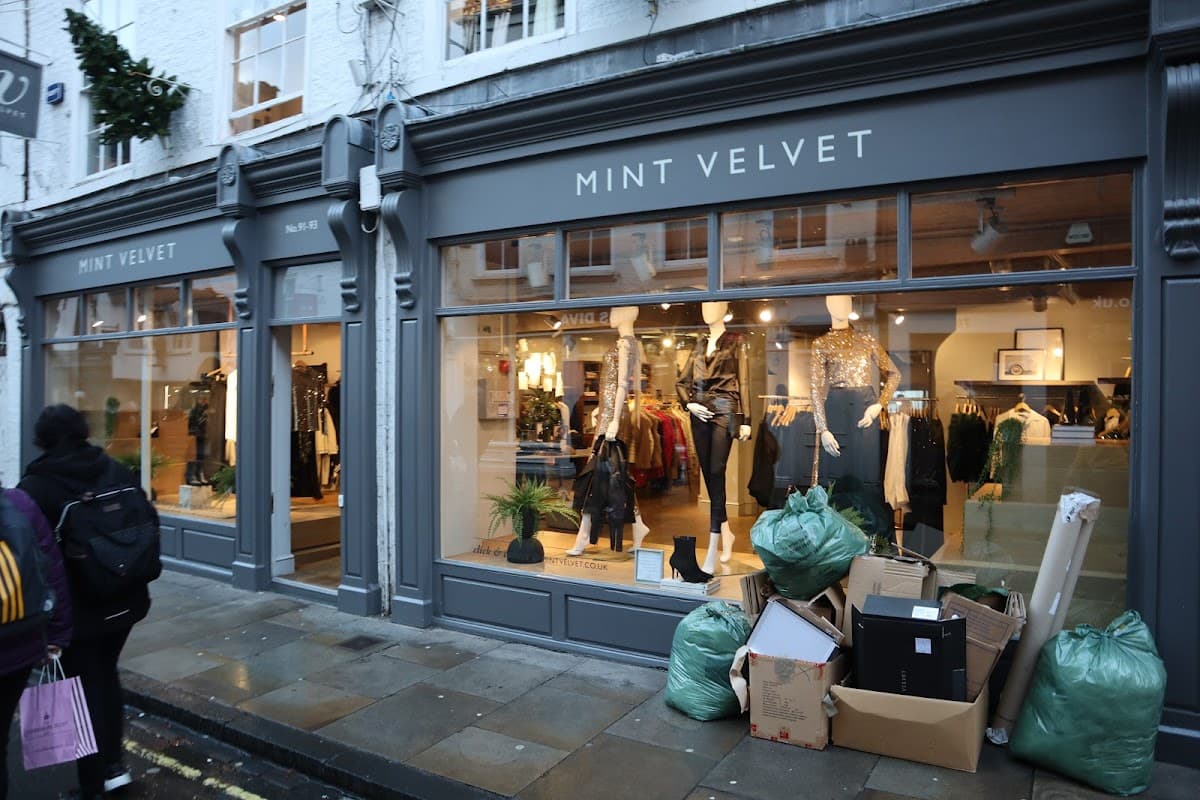 Mint Velvet shop front in York, featuring stylish clothing displays and green bags piled outside.