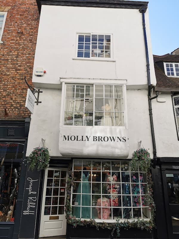 Molly Browns shopfront featuring elegant dresses, large windows, and floral decorations in York, Yorkshire.