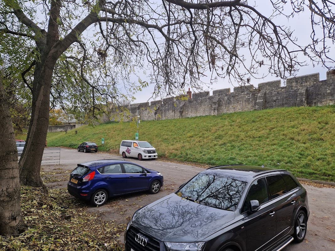 Monkbar Mews Public Car Park with parked cars, a grassy area, and York's historic city walls in the background.