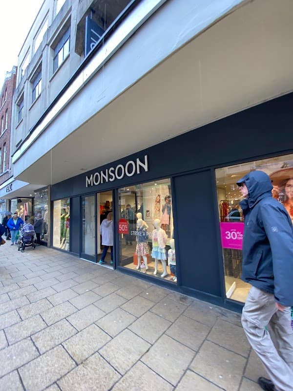 Monsoon shop front with large windows displaying clothing, shoppers walking by on a rainy day in York.