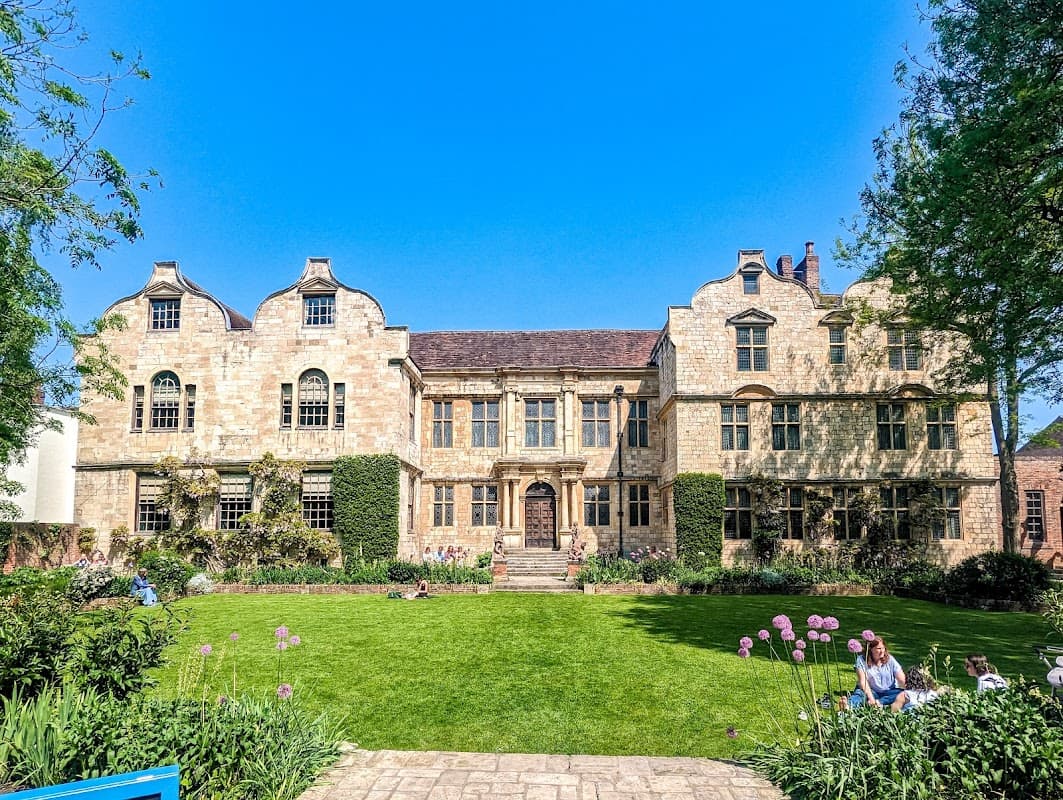 Historic Treasurer's House in York, featuring stone architecture, manicured gardens, and blue sky. Visitors relax on the lawn.
