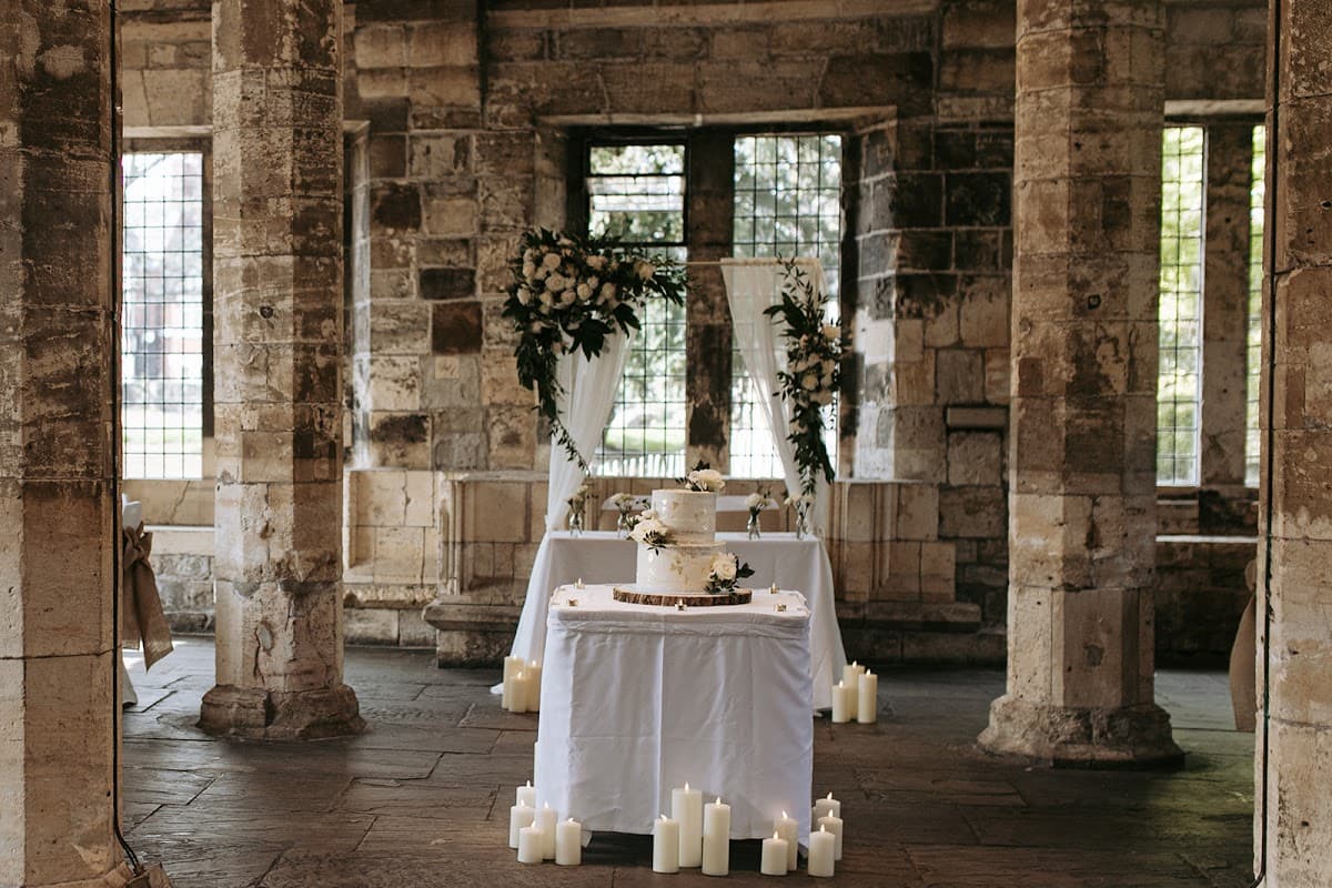 Elegant wedding setup with a decorated cake, floral arrangements, and candles in a historic stone building.