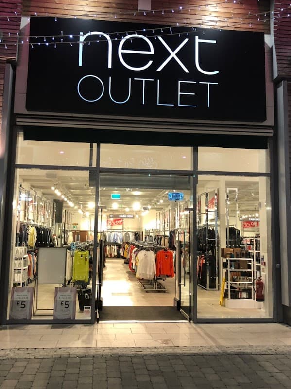Brightly lit storefront of Next Outlet featuring various clothing displays and promotional signage in York, Yorkshire.