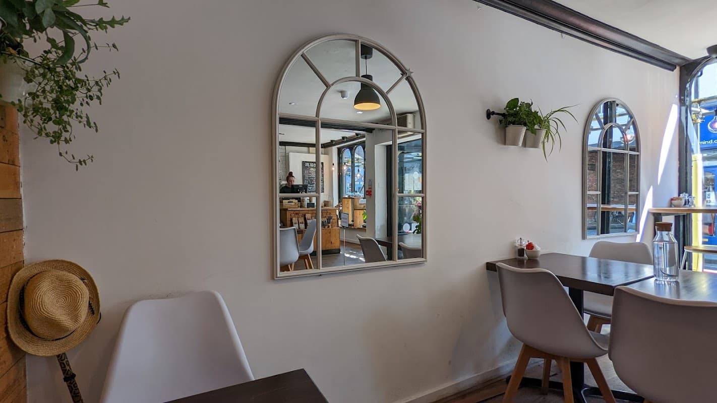 Cozy cafe interior with a large mirror, wooden tables, plants, and a glimpse of the counter in York, Yorkshire.